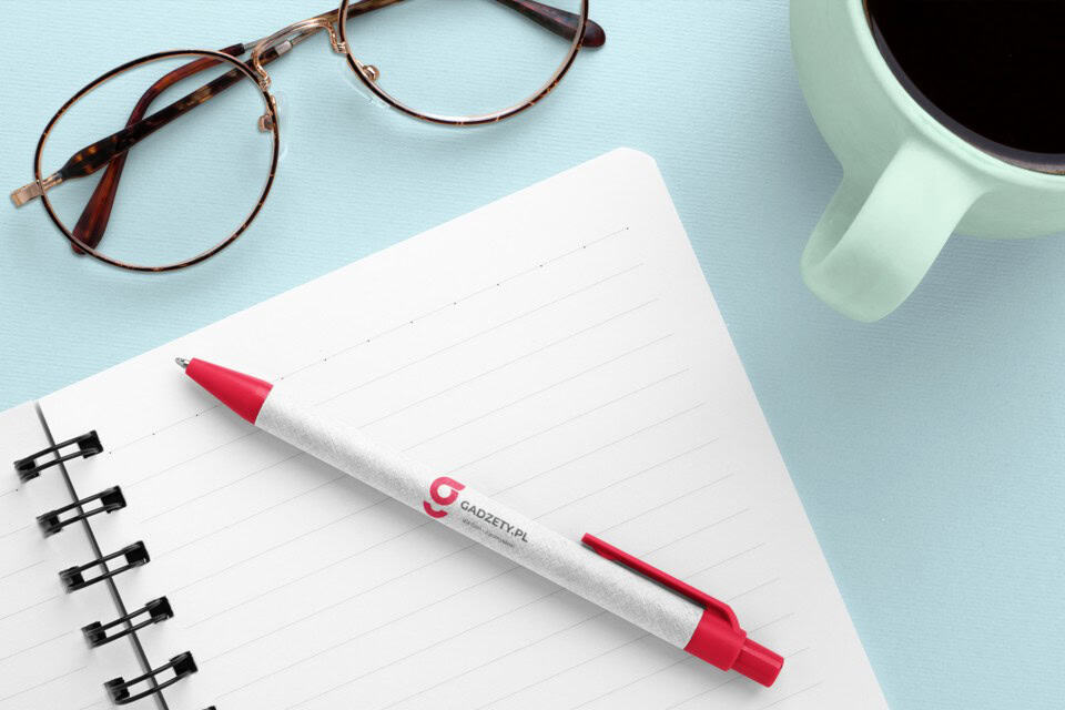 Długopis reklamowy z logo gadzety.pl, notatnik i okulary na biurku, kubek z kawą, gadżety promocyjne, zestaw do biura.
