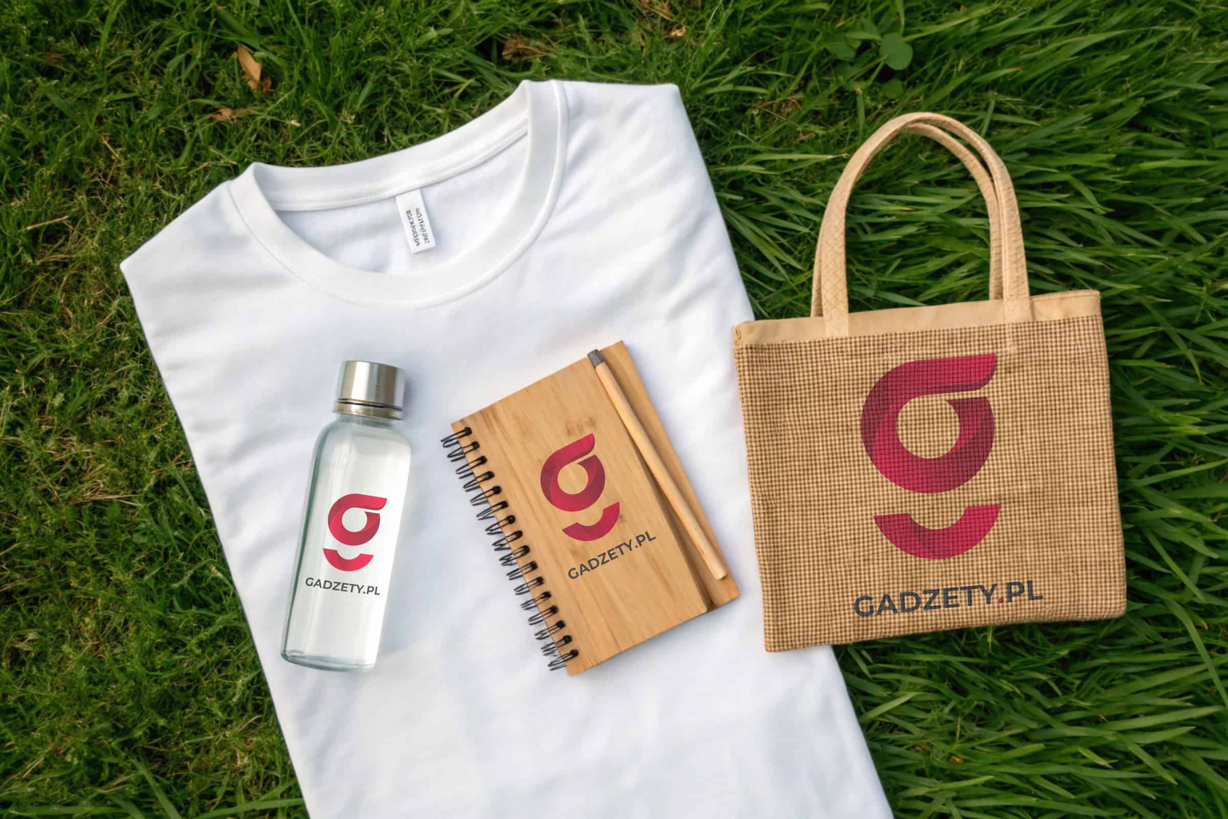 Logo gadżety.pl na butelce, torbie i notatniku z nadrukiem, na trawie.