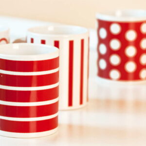 Kolorowe kubki z nadrukami w czerwonych wzorach i groszkach na świąteczne gadżety.