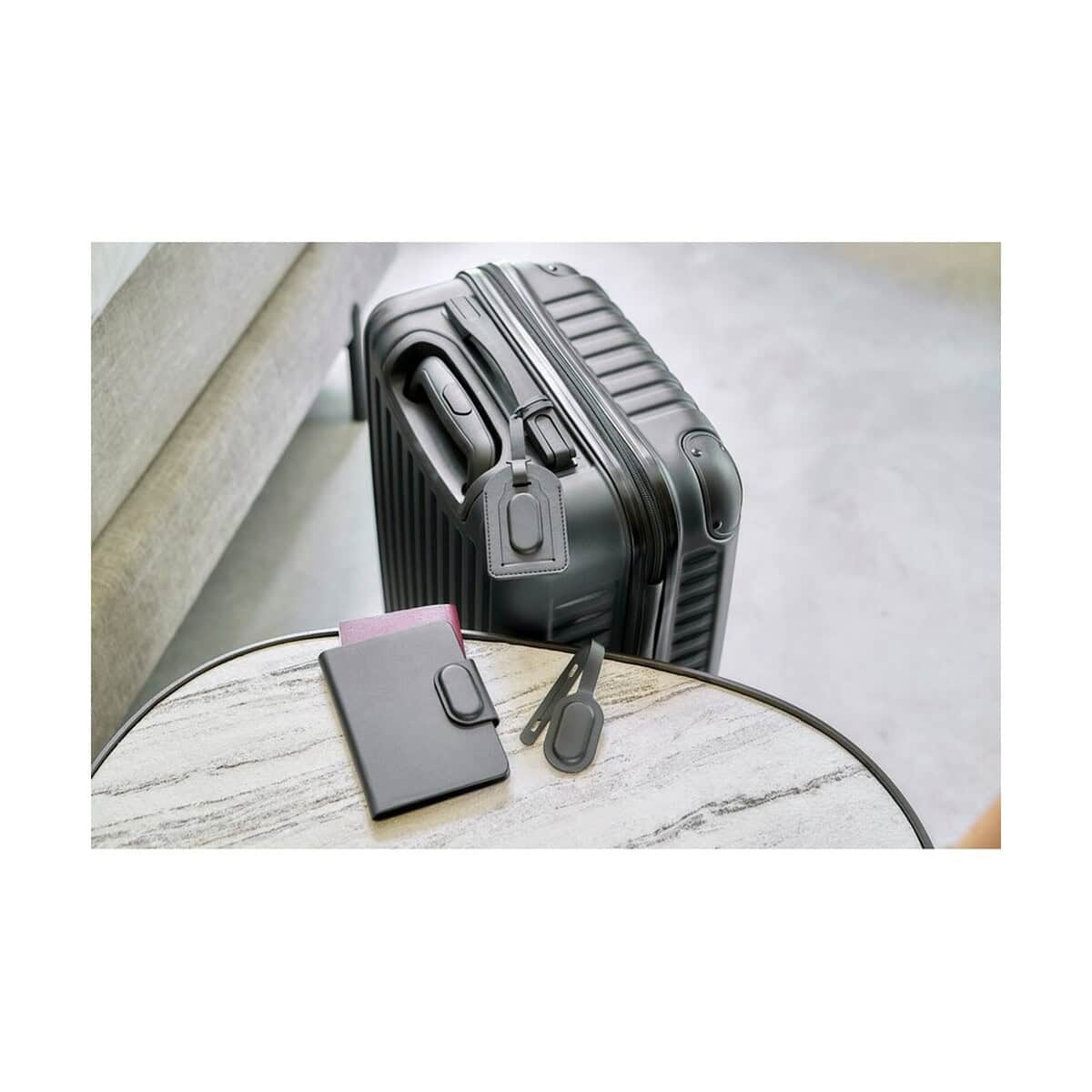 Lokalizatory kluczy z logo – etui na paszport z lokalizatorem VA517-03_ATM02 Czarny zestaw akcesoriów do bagażu, obejmujący torbę i etui na paszport, na tle walizki na podróż.