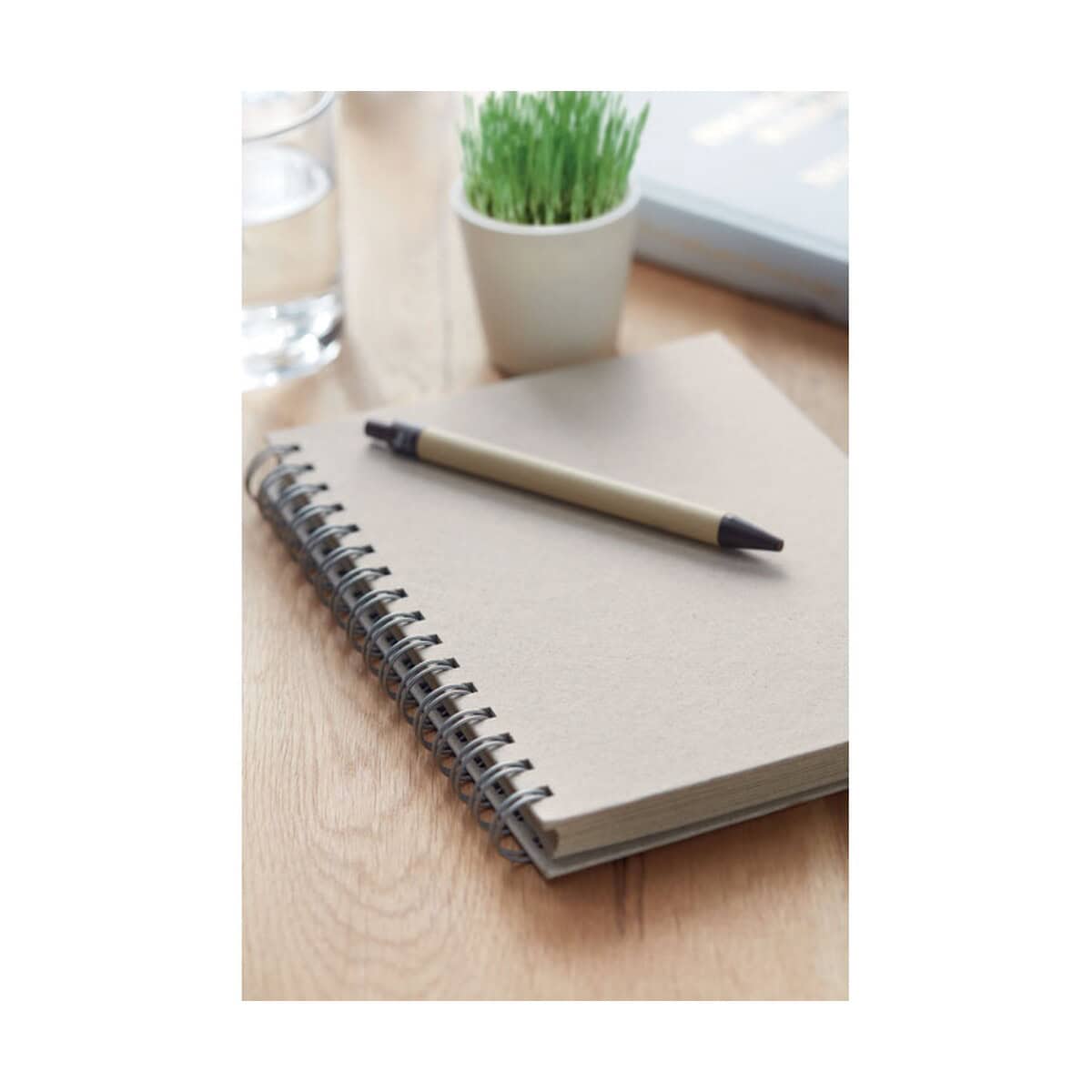 Notatniki z logo – notesa5 kratkę, papier z trawy grass book mo6541-13-ambiant Notes: The provided URL and the context suggest the image is related to gadgets (gadżety). However, this specific image features a notebook, pen, plant, and glass of water, which may not directly relate to