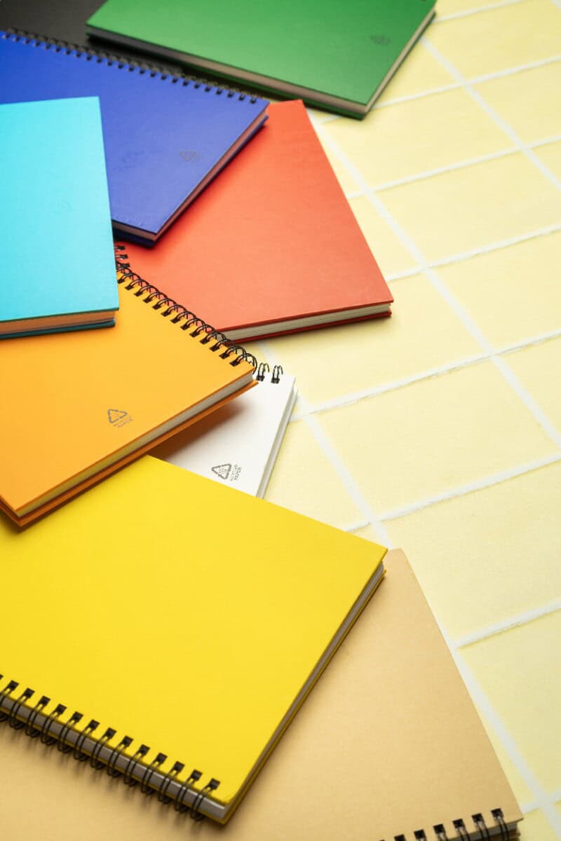 Notatniki z logo – strobus a5 notes AP800194-00__DG Kolorowe notesy i notes z spiralą na tle jasnych płytek ceramicznych.