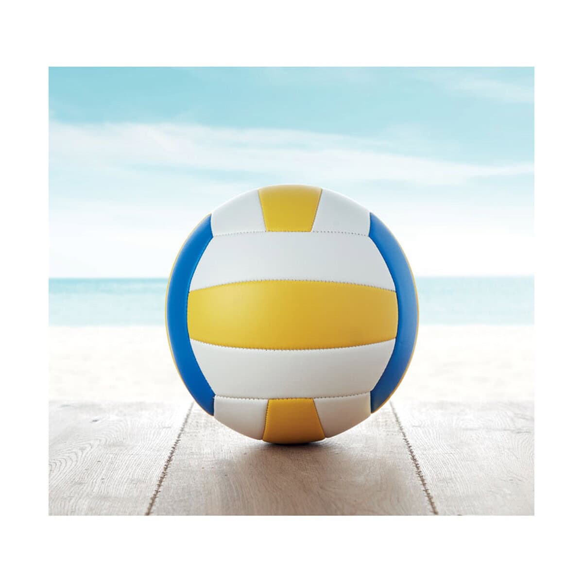Piłki z logo – piłka do siatkówki volley mo9854-99-ambiant Piłka plażowa w kolorach niebiesko-żółtych na plaży z widokiem na morze.