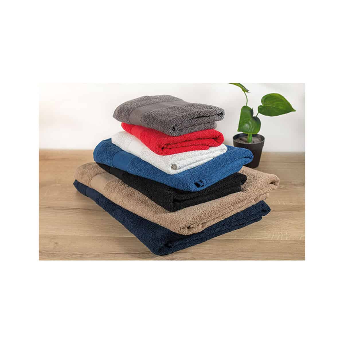 Ręczniki z logo – ręcznik baweł. organ. 100×50 terry mo9931-03-ambiant Zestaw ręczników z mikrofibry w różnych kolorach na drewnianym stole z rośliną.