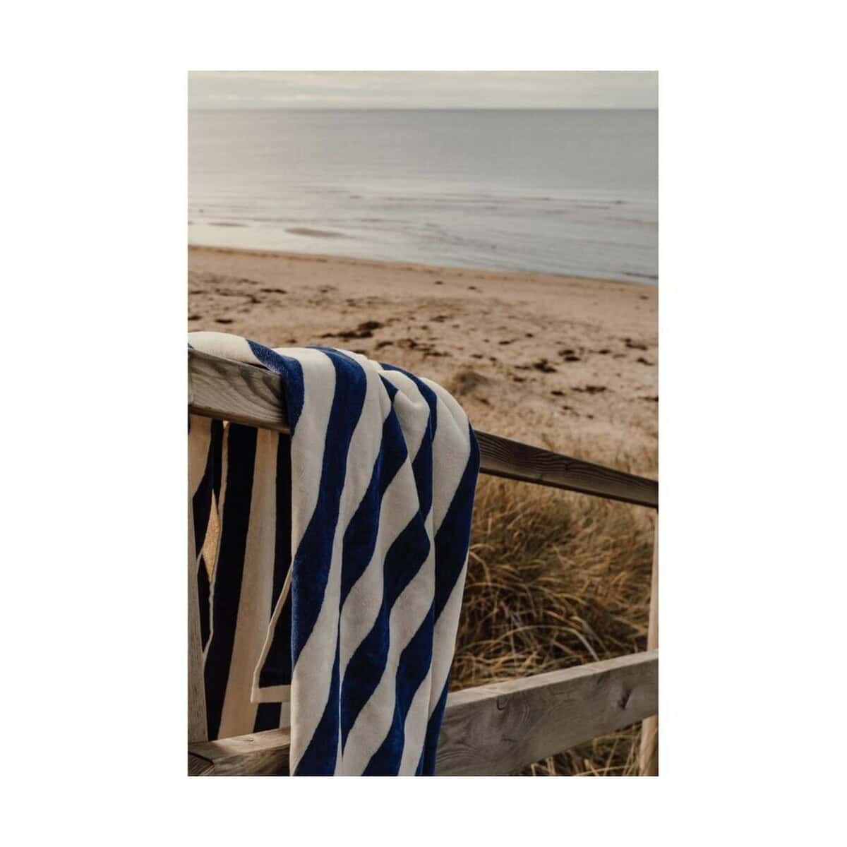 Letnia plaża z ręcznikiem na drewnianym ogrodzeniu, relaks nad morzem. Plażowy ręcznik na drewnianym ogrodzeniu z widokiem na morze i piasek.