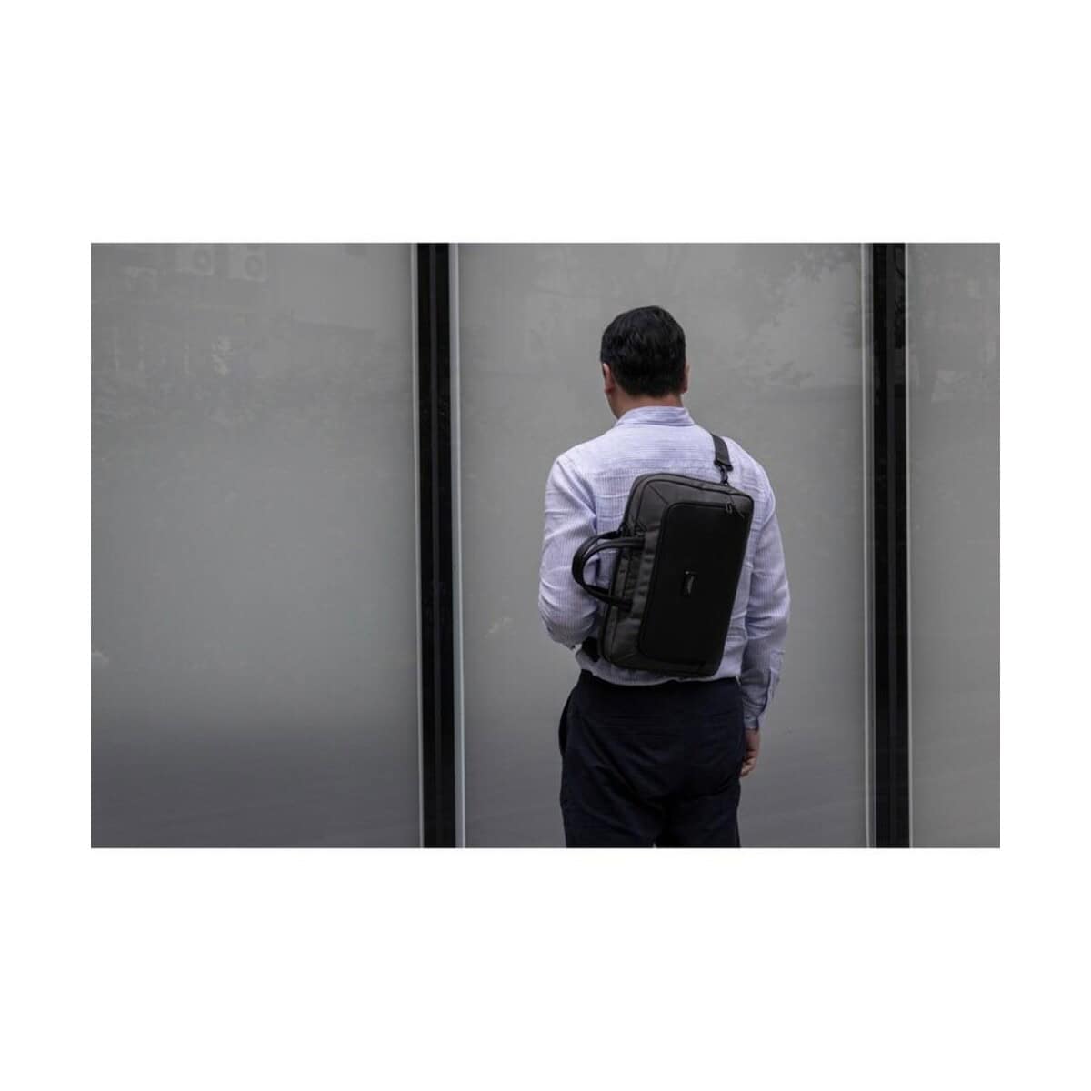 Gadżety dla podróżnych Pracownik z plecakiem na tle szklanych drzwi, symbolizujący podróże i mobilność.